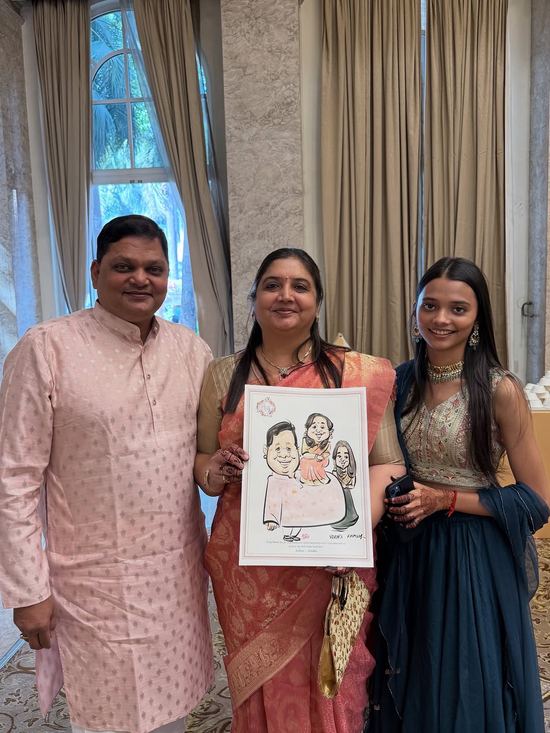 Vora family of three holding a live family caricature at a wedding function