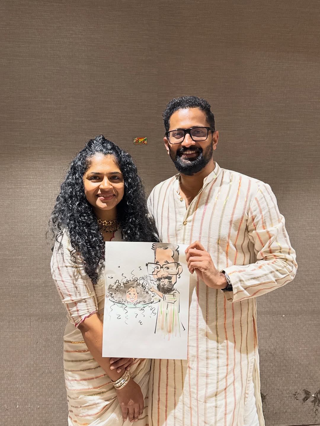 Curly-haired couple holding a live caricature drawn at their celebration